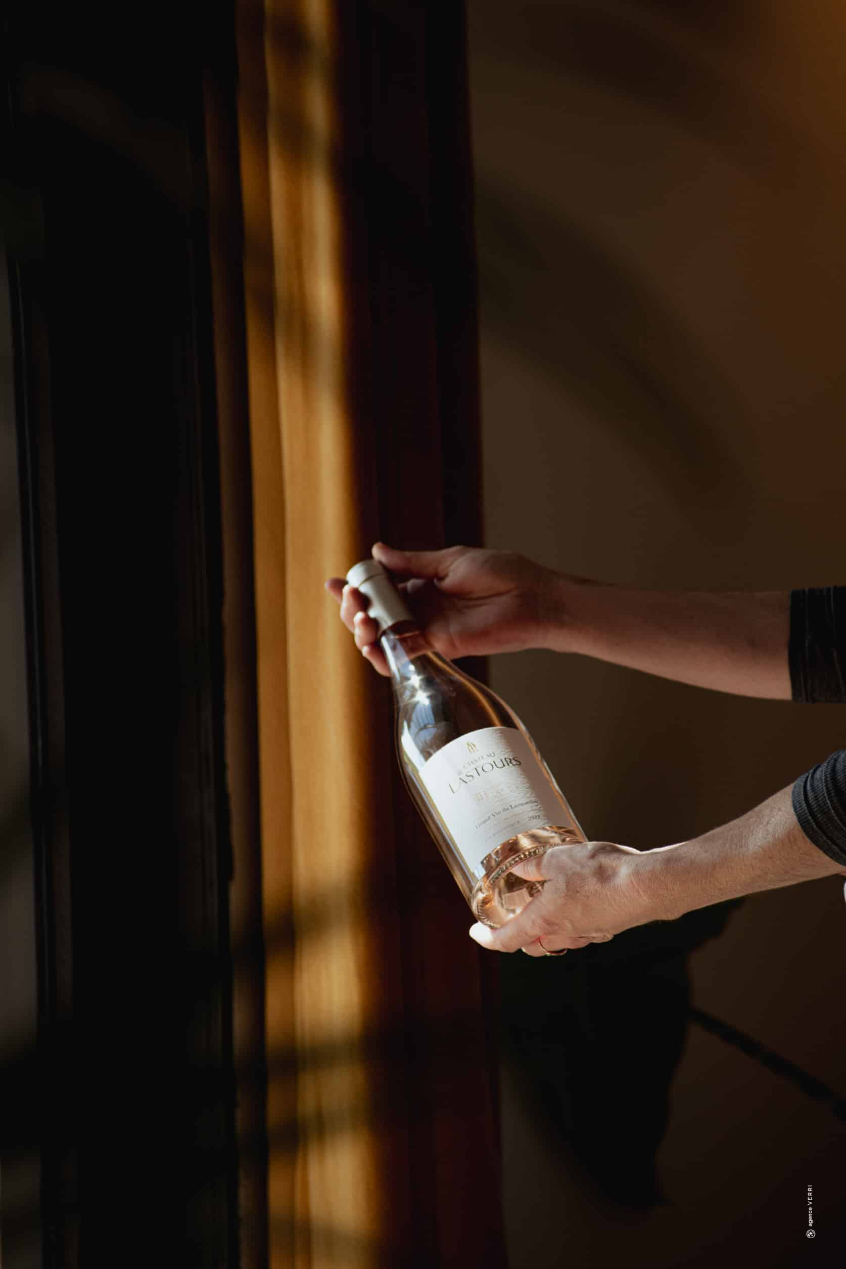 Bouteille de vin rosé Château de Lastours tenue à la lumière naturelle, devant un rideau ocre