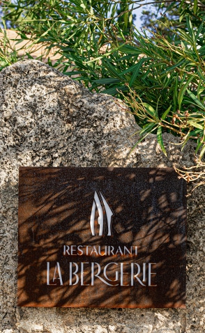 Enseigne en métal du restaurant La Bergerie au Château de Lastours fixée sur un mur en pierre